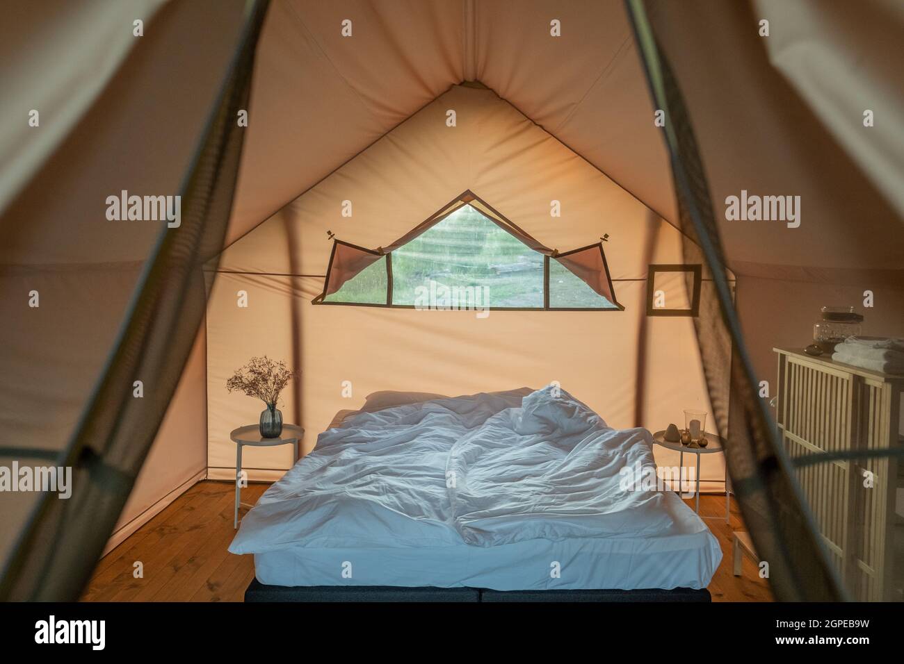Undone double bed between small round tables inside bedroom of glamping house Stock Photo