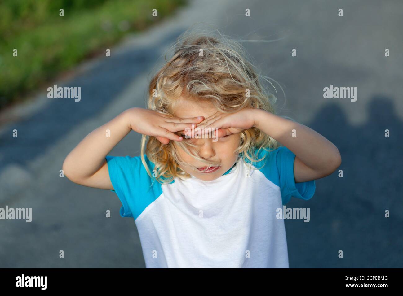 Little boy covering his eyes by the sun, on a sunny day Stock Photo