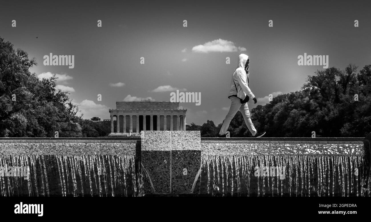 Black and white image of lone person in white walking across reflecting pool waterfall in Washington DC with view of Lincoln memorial. Stock Photo