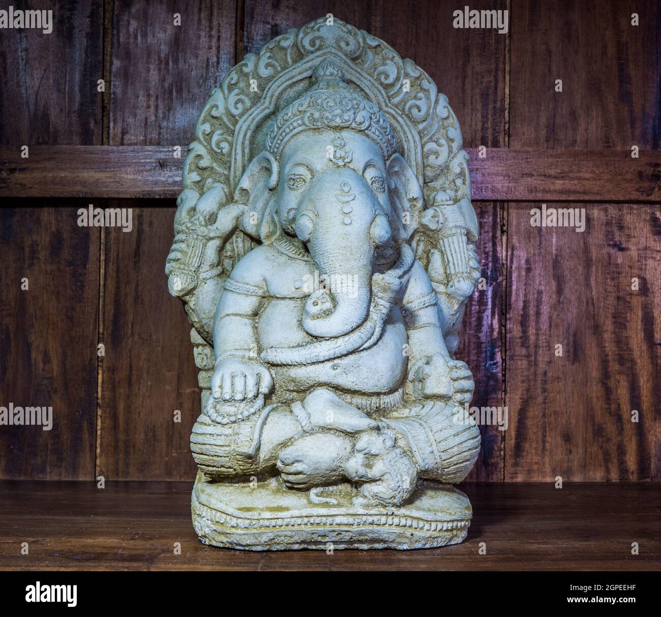 A stone ornament / statue on a shelf in an old wooden cabinet, of Ganesh / Ganesha, the elephant headed Hindu god of beginnings. Stock Photo