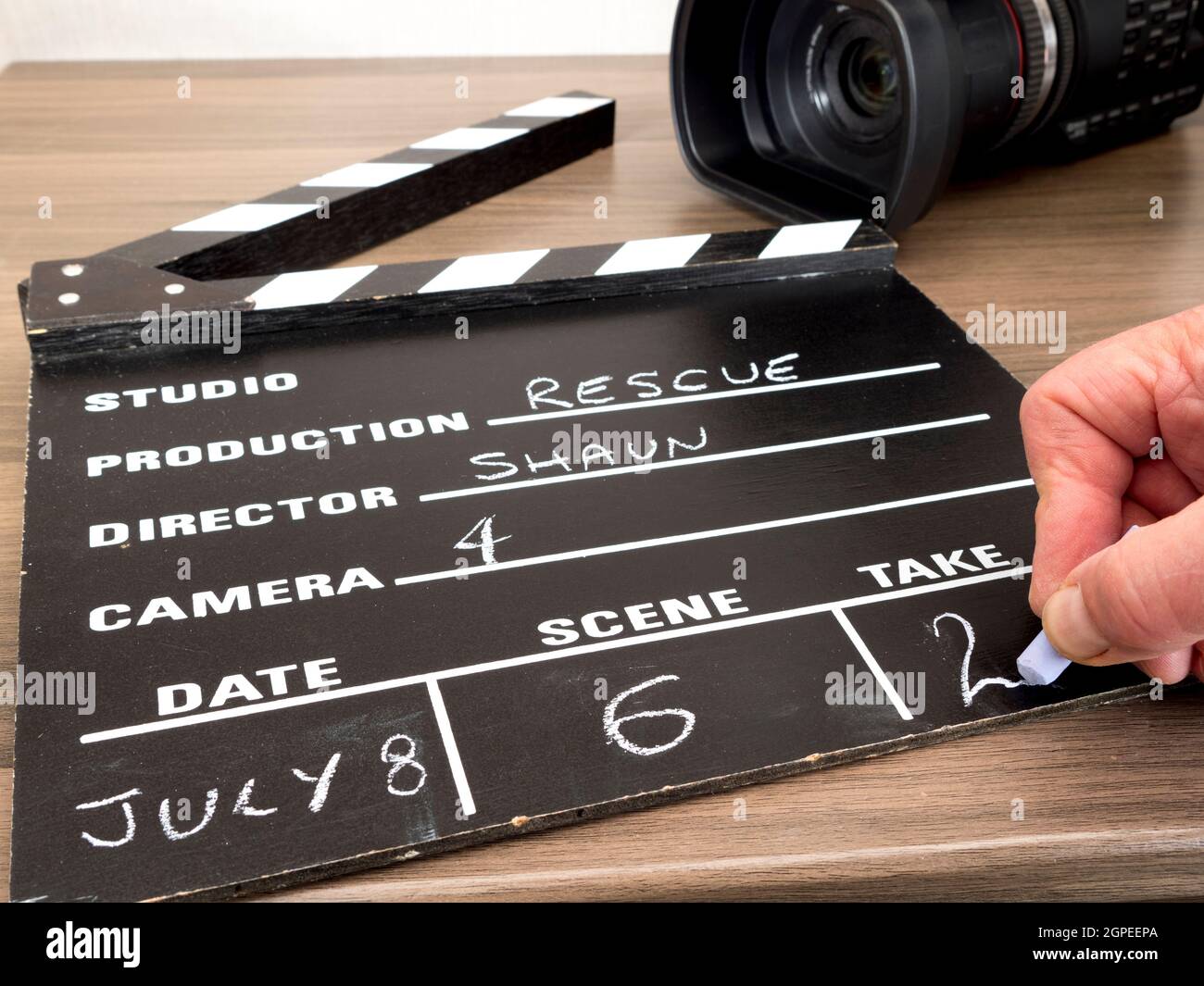 Closeup POV shot of a man's hand chalking Take 2 on a traditional clapper board, with a video camera behind. Stock Photo