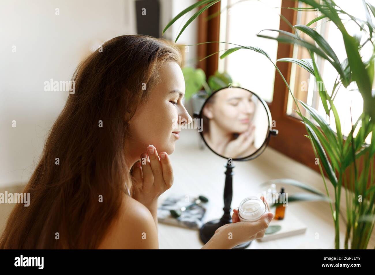Beauty girl looking at mirror while touching her face and applying ...