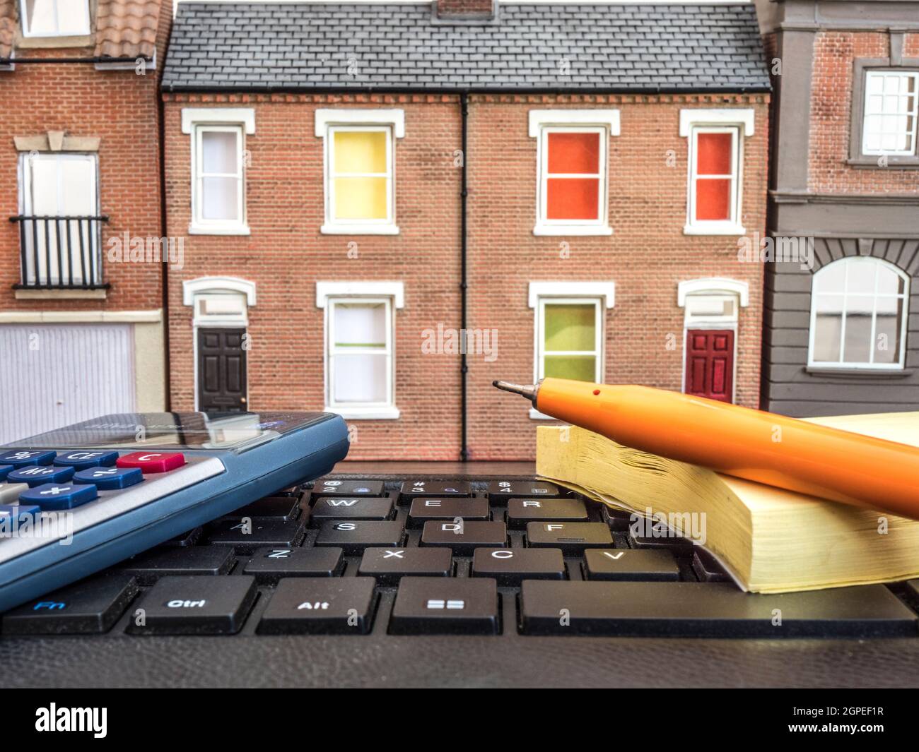 Realtor / estate agent concept: A portable keyboard in front of a line of model / toy buildings, with calculator, pen and note pad. Stock Photo