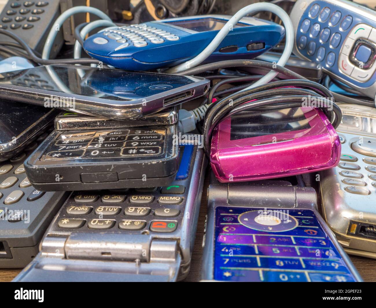 Closeup of a pile of old mobile phones and chargers – old technology ranging from the late 1990s up to the period before the advent of smartphones. Stock Photo