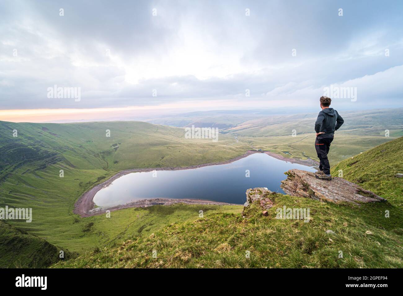 Man overlooking Llyn y Fan Fach lake. Brecon Beacons National Park. Black Mountain, Carmarthenshire, South Wales, the United Kingdom. Hiking in the UK concept. Stock Photo