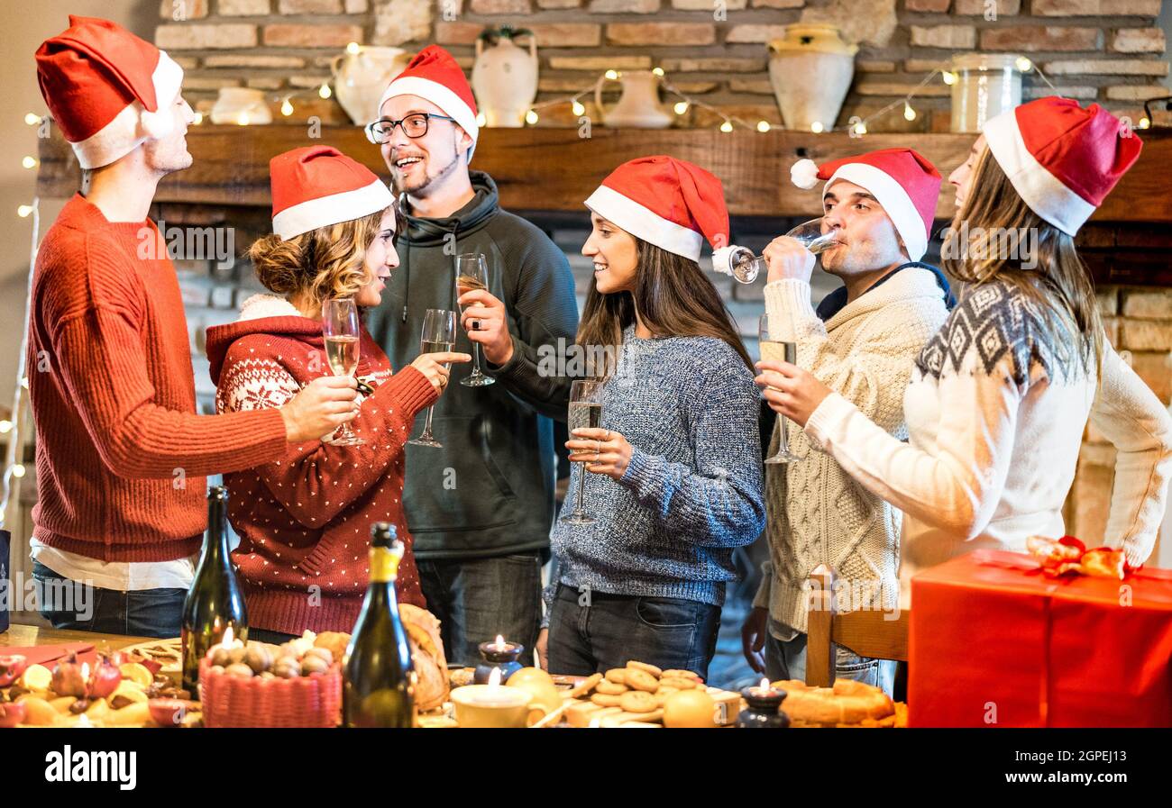 Friends group with santa hats celebrating Christmas with champagne wine toast at home dinner - Winter holidays concept with young people talking Stock Photo