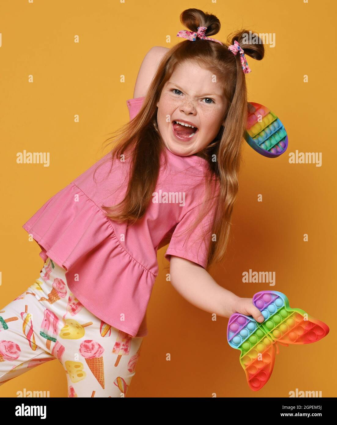Frolic, active kid girl in colorful clothes plays with two sensory rainbow color toys - pop it in hands Stock Photo