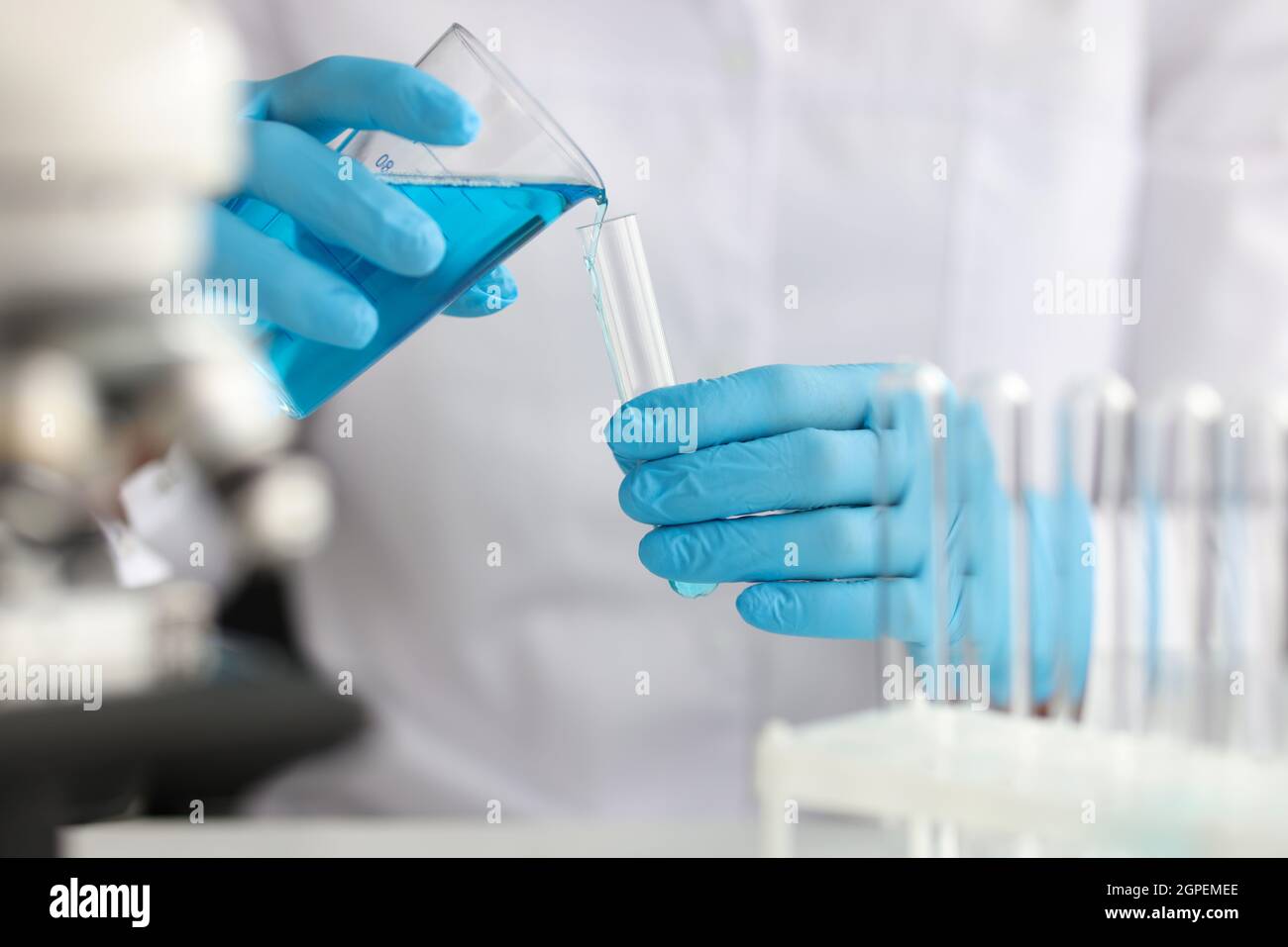 Scientist with gloves pours blue liquid into test tube in laboratory ...