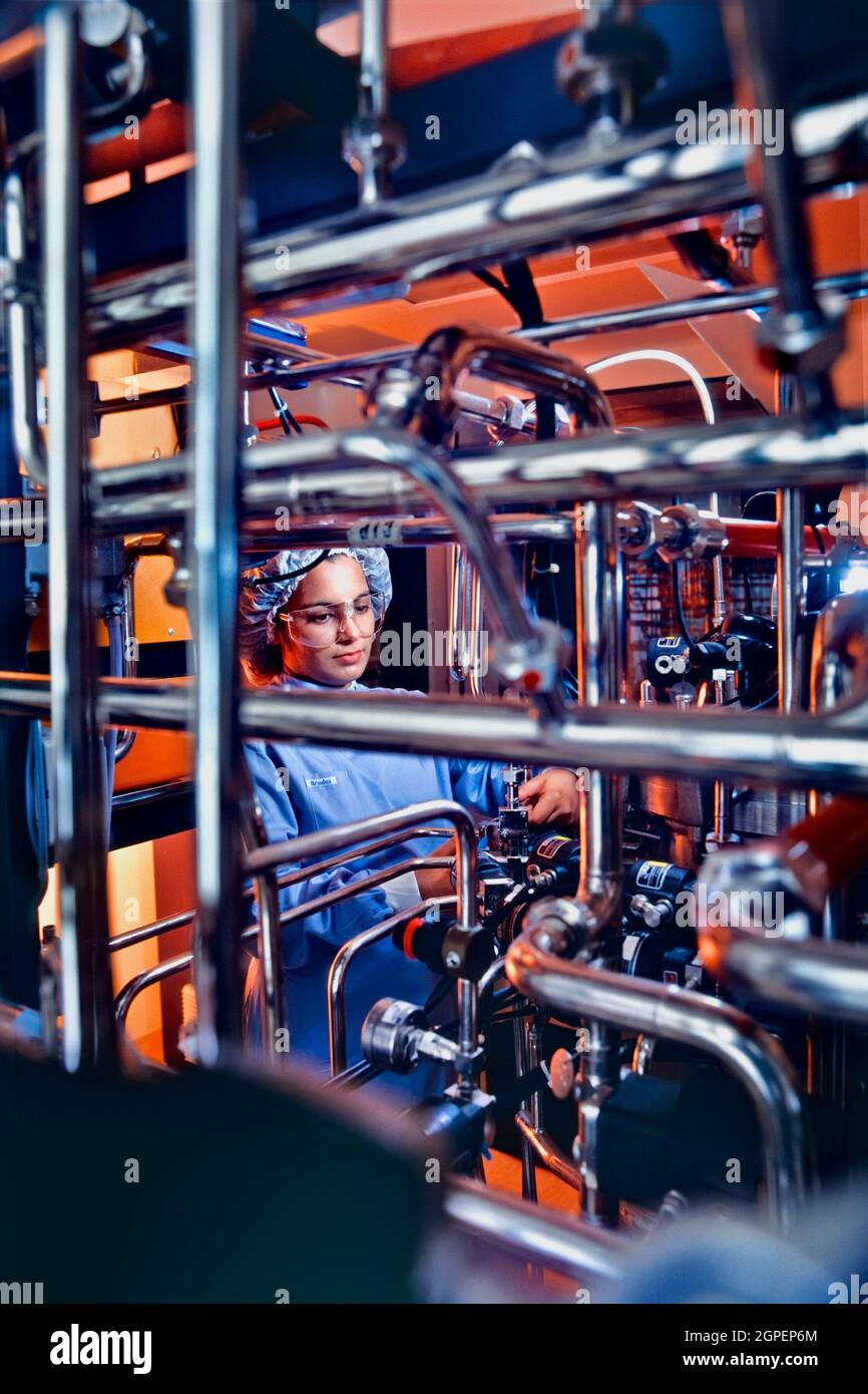 Woman technician wearing clean-room clothing adjusting fermentor culturing yeast cells which are genetically engineered to produce proteins designed f Stock Photo