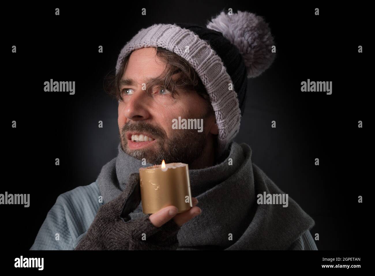 Middle-aged Caucasian man wearing fingerless gloves and a knitted hat and holding a candle Stock Photo