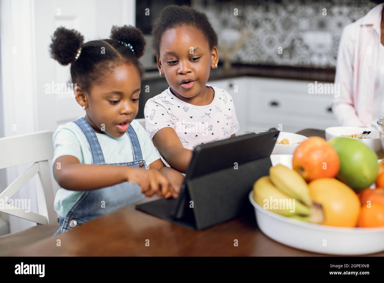 Pretty african american girls watching cartoons on digital tablet while  sitting together on bright kitchen. Two sisters using modern gadgets during  breakfast at home. Children and technologies concept Stock Photo - Alamy