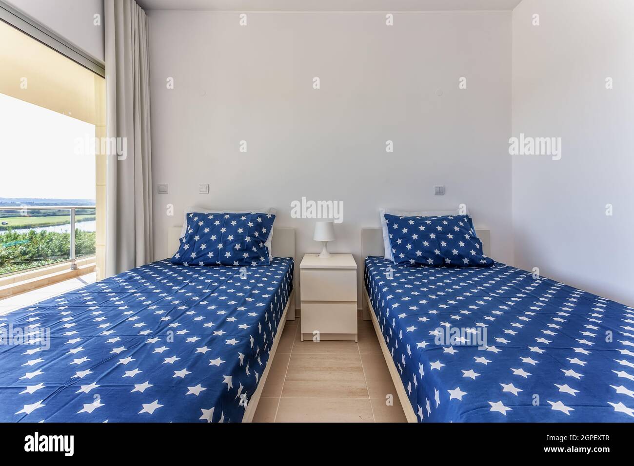 The interior of a traditional bedroom, with two beds covered with blue bedspreads with stars. Stock Photo