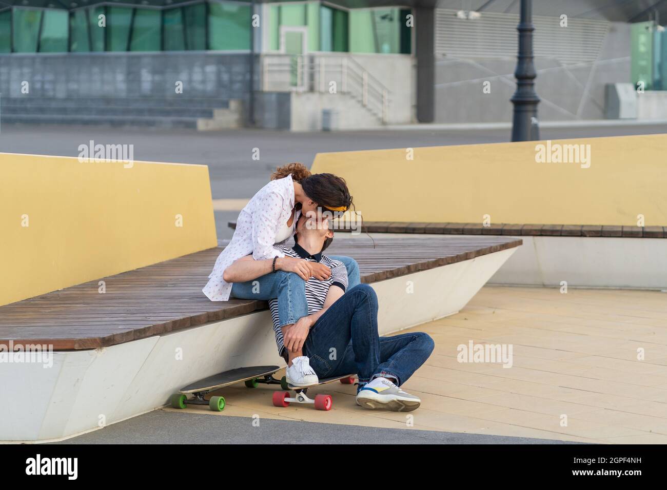 Couple of skaters kissing sit on longboard together outdoors in urban space. Youth, romance and love Stock Photo