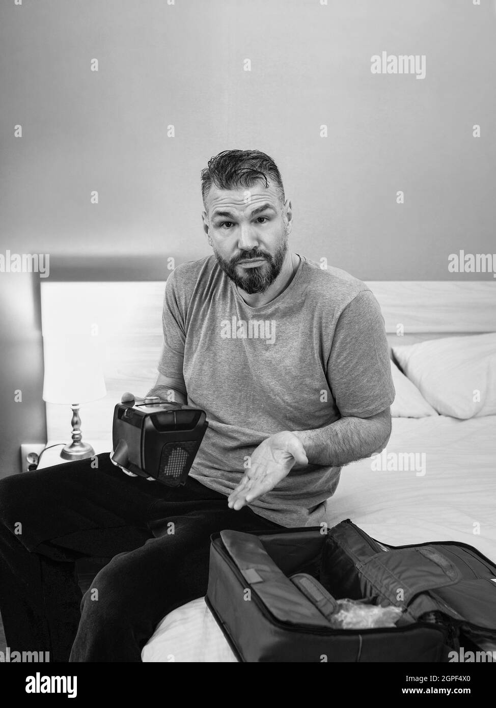 Unhappy shocked man with chronic breathing issues surprised by using  CPAP machine sitting on the bed in bedroom. Stock Photo