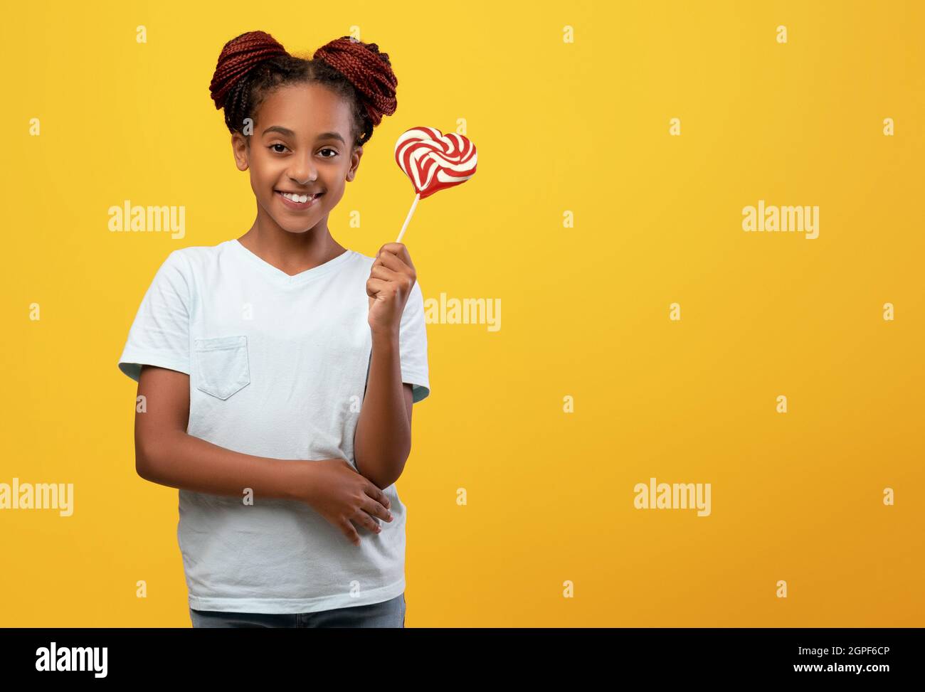 Pretty black girl holding candy, yellow studio background Stock Photo