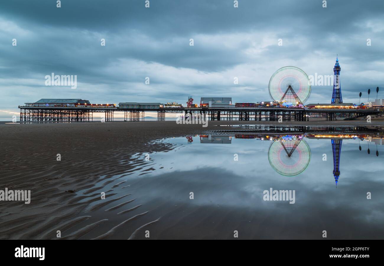 A long exposure of the Ferris wheel spinning on the Central Pier on Blackpool beach seen at twilight in September 2021 as Blackpool Tower is lit up in Stock Photo