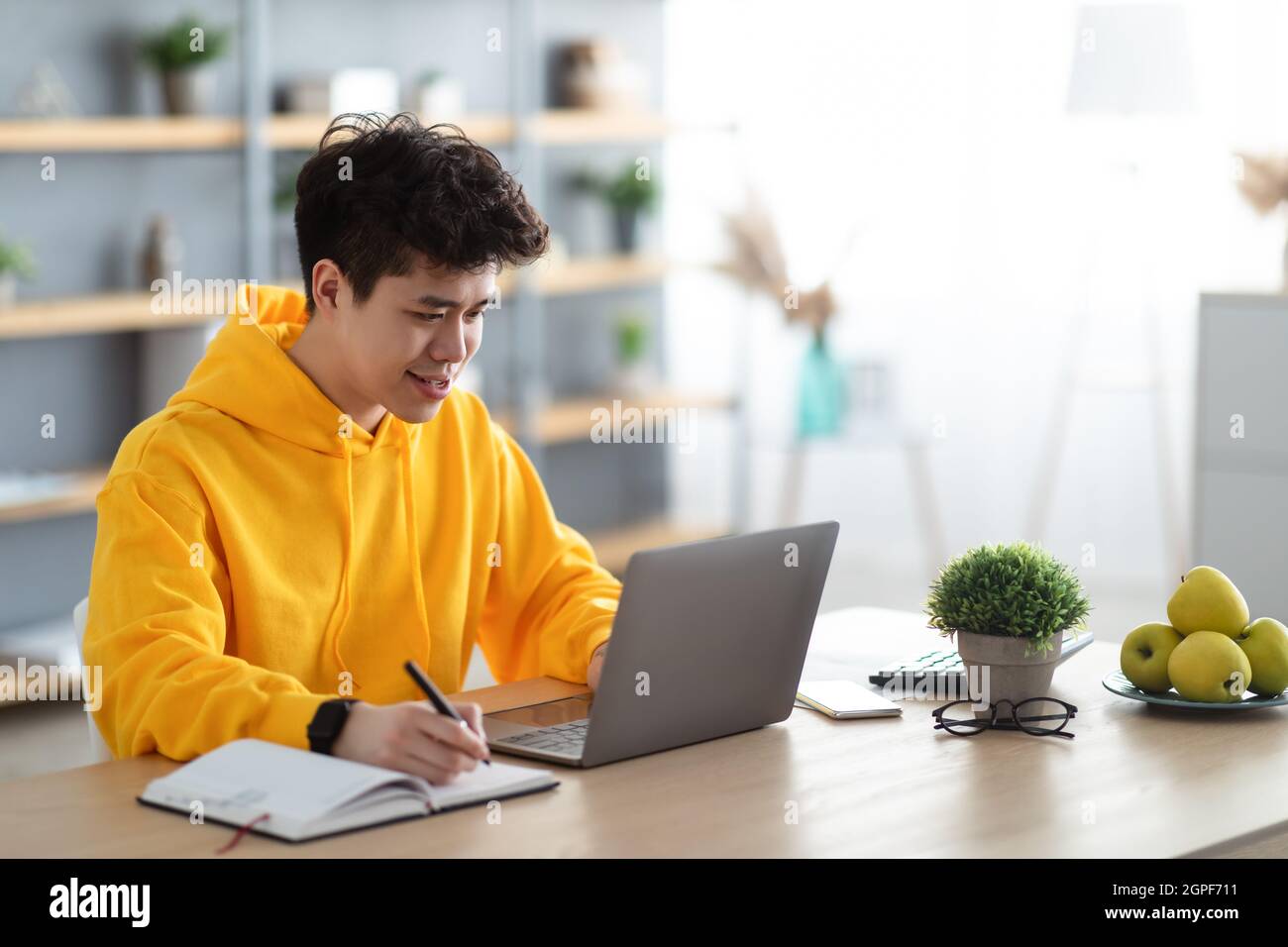 Smiling asian man working on laptop and writing Stock Photo