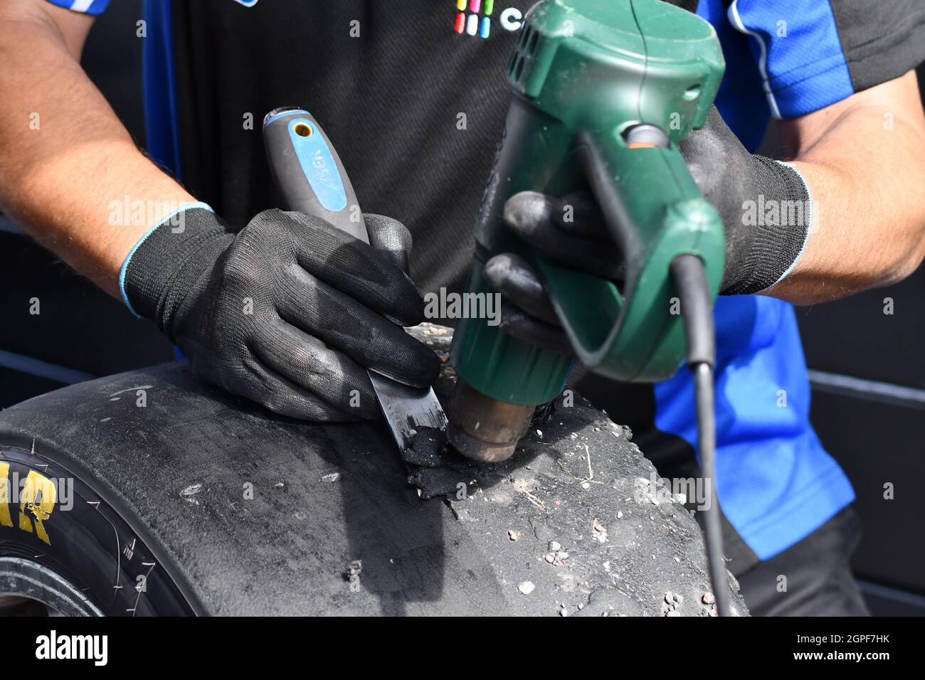 A team mechanic removing the worn rubber with a heat gun from a recently run slick racing car tyre Stock Photo