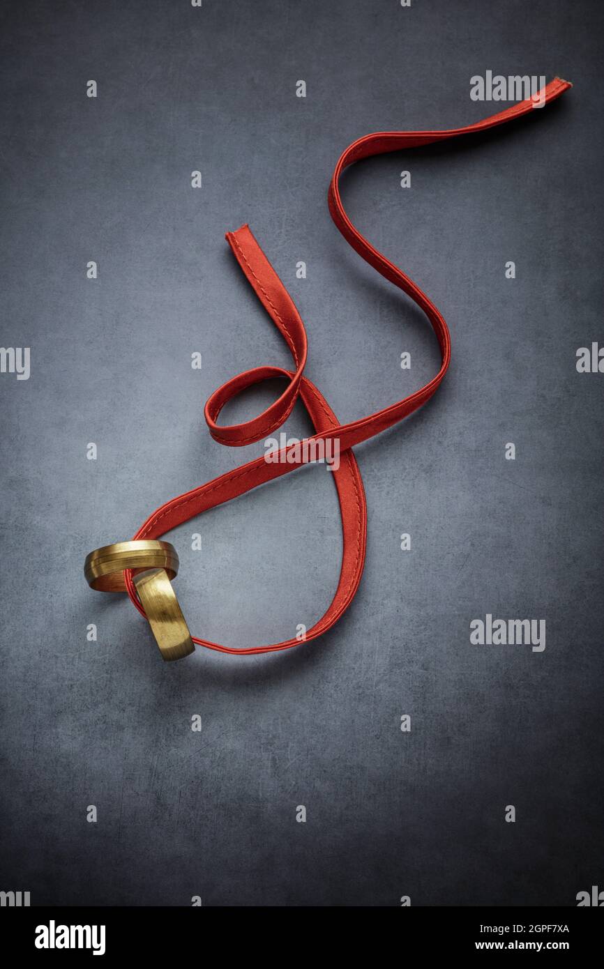 Two rings and a red ribbon on dark background Stock Photo