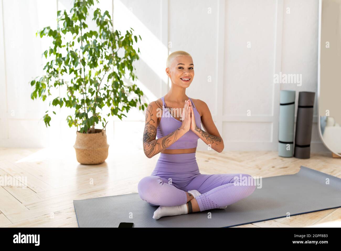 Peaceful young lady meditating at home, sitting in lotus position and smiling to camera, living room, copy space Stock Photo