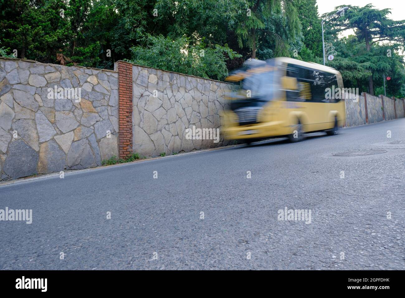 Beyoglu, Istanbul, Turkey - 06.27.2021: an out of focus yellow passenger minibus coming down from straight asphalt downhill road near some stone walls Stock Photo