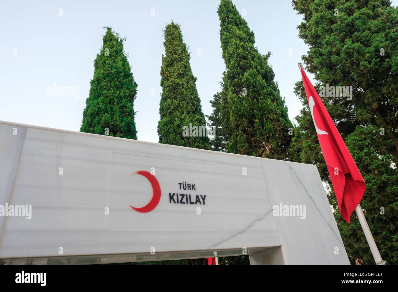 Beyoglu, Istanbul, Turkey - 06.27.2021: logo of Turkish Red Crescent (Turk Kizilay) on marble near Turkish flag and a lot of trees under blue sky from Stock Photo