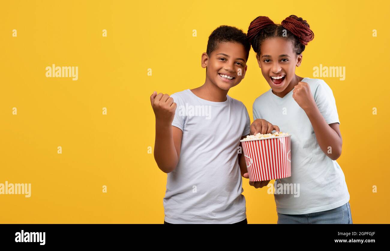 Emotional afro-american siblings watching cartoon together, eating popcorn Stock Photo