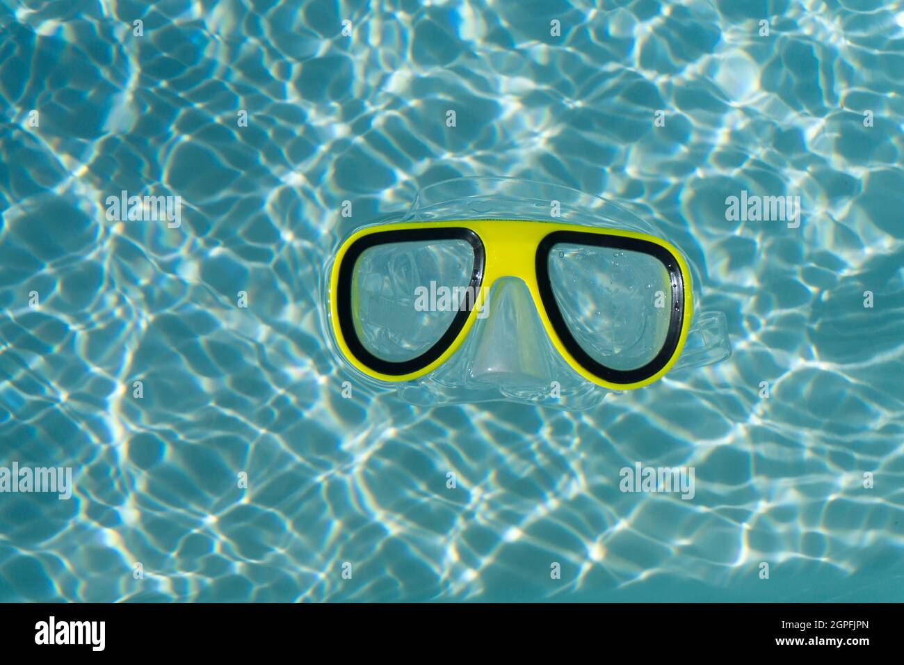 A yellow snorkel swimming goggles floating in a clear blue rippled