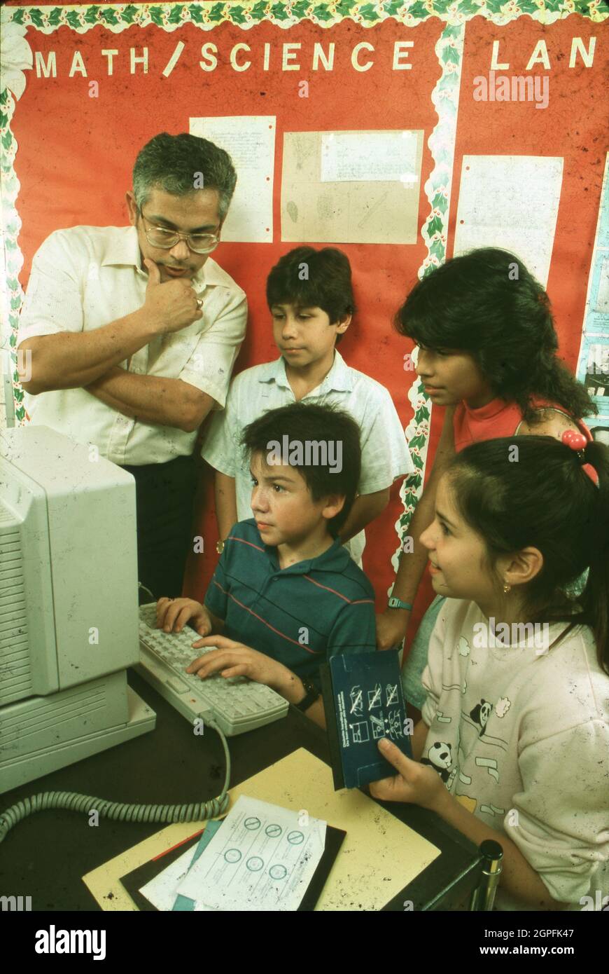 Austin Texas USA, January, 1990: Hispanic fifth grader works on computer as teacher and fellow students look on at Joslin Elementary School. MR ES-035  ©Bob Daemmrich Stock Photo