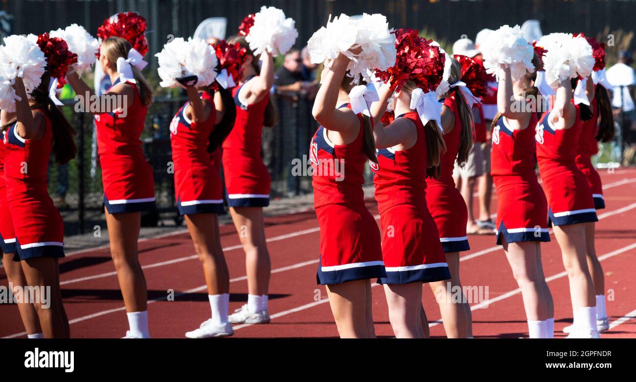 High school cheerleaders holding their pompoms in the air while cheering during a football game. Stock Photo