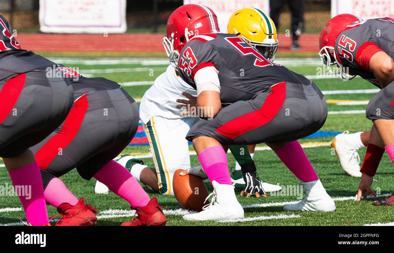 A high school football center with his hand on the ball set and ready