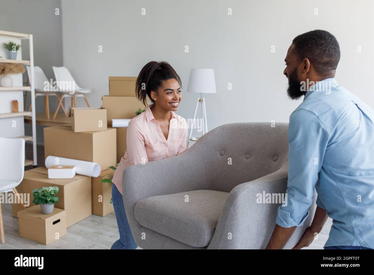 Happy millennial african american husband and wife carry armchair in ...