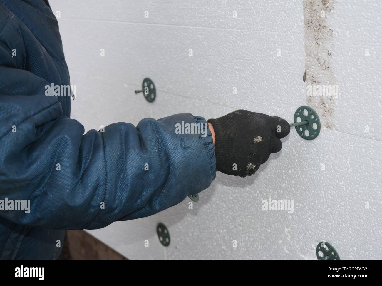 Builder installing foam insulation board with plastic nails and hammer