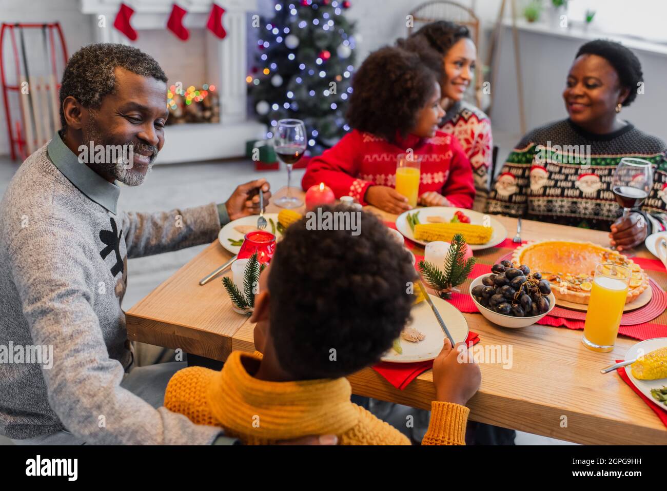 happy african american man talking to grandson near christmas dinner with blurred family Stock Photo