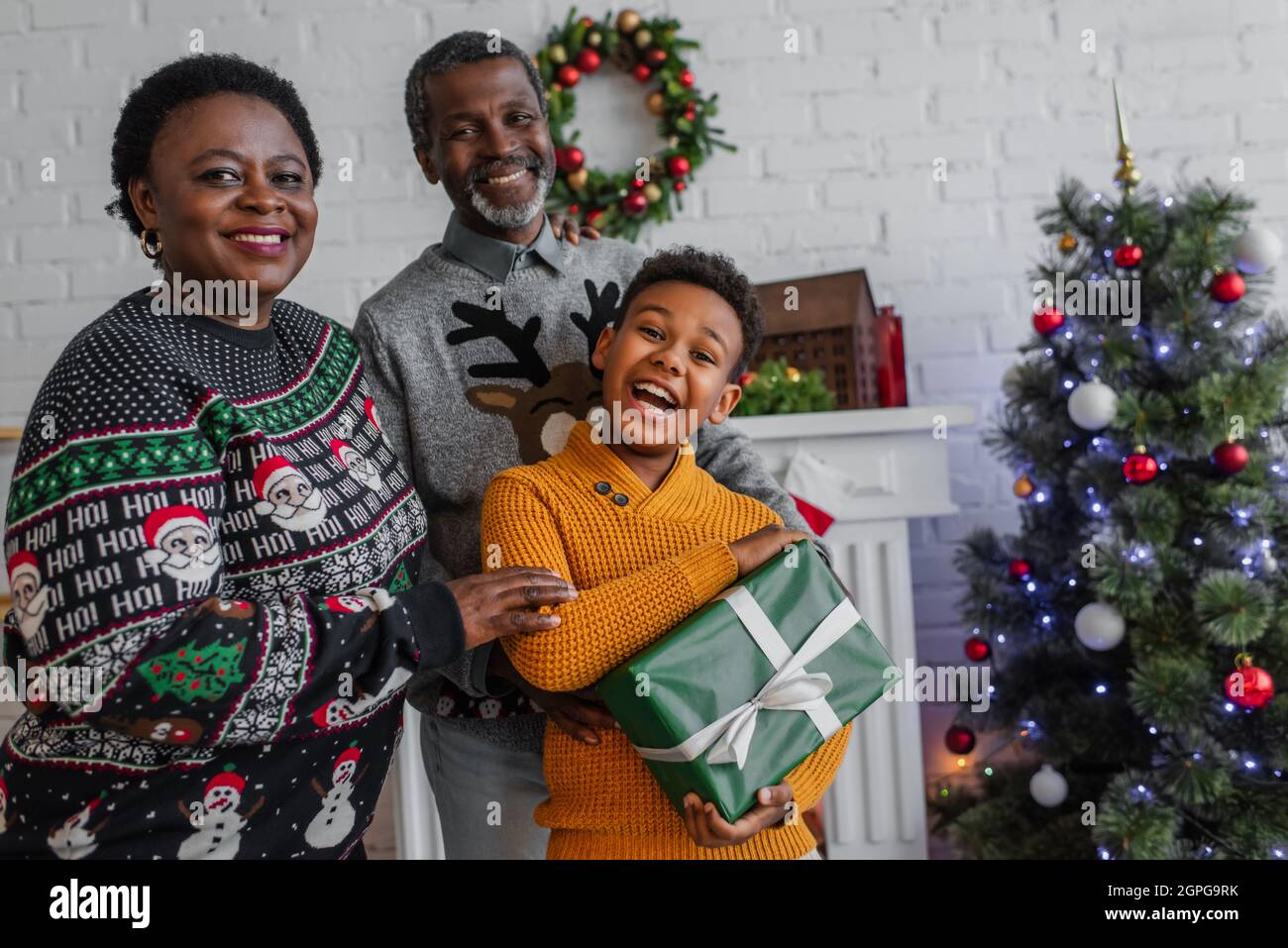 excited african american boy holding christmas gift near happy grandparents and blurred christmas tree Stock Photo