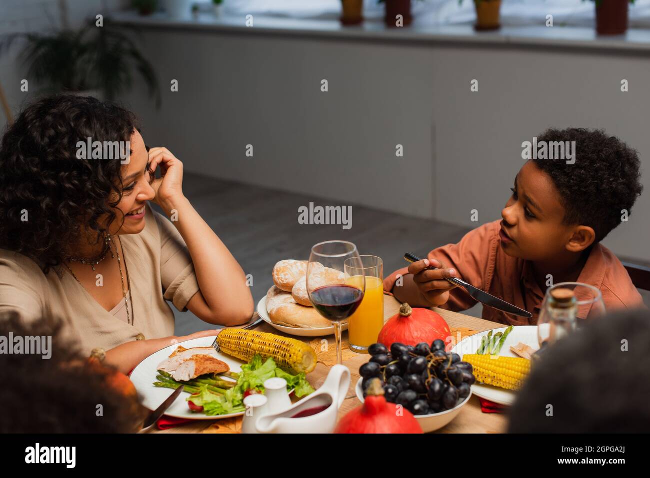 happy african american woman talking to son during thanksgiving dinner with blurred family Stock Photo