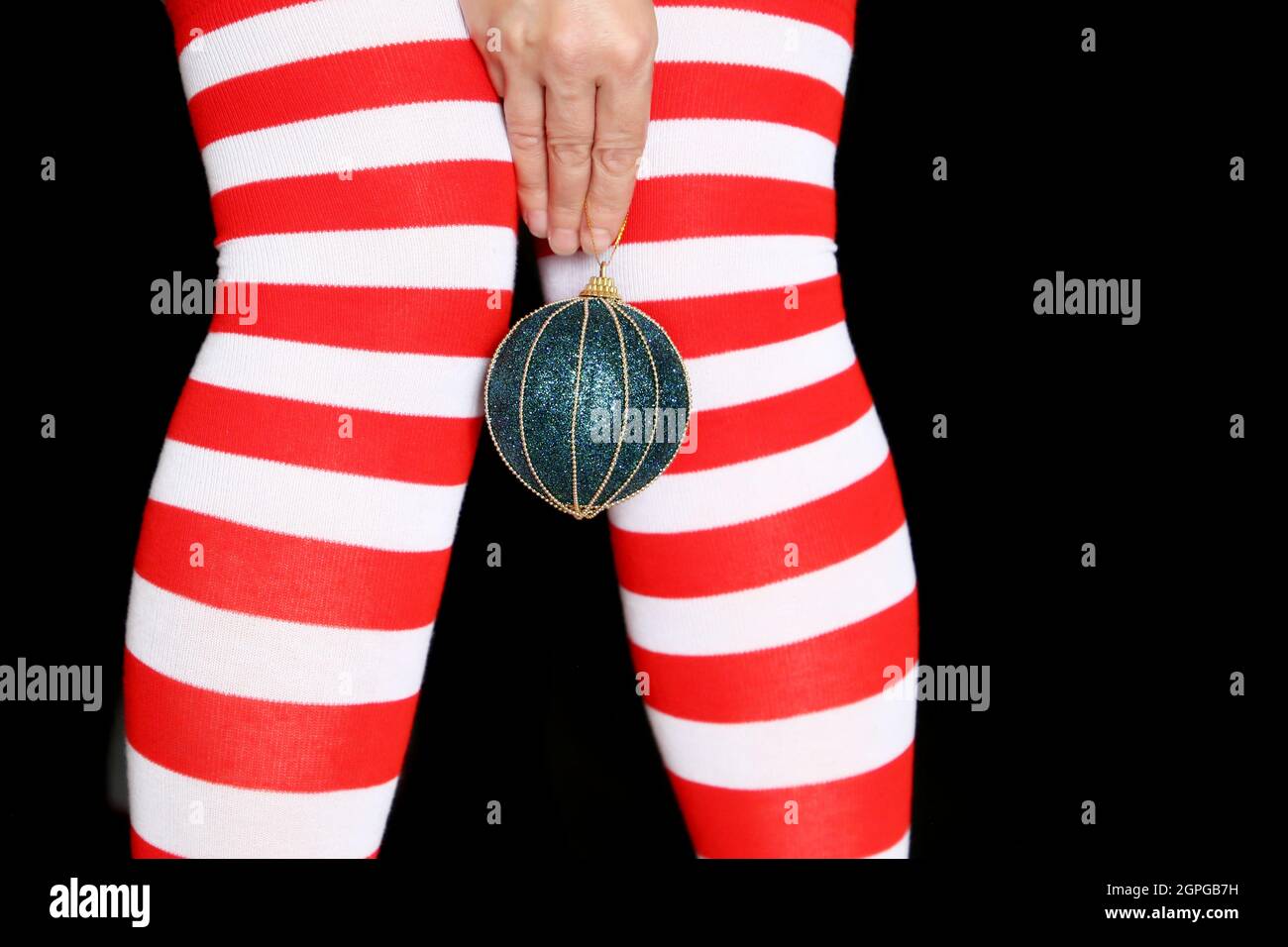 Female legs in Christmas knee socks on black background. Woman with toy ball in hand, concept of New Year celebration, girl in Santa costume Stock Photo