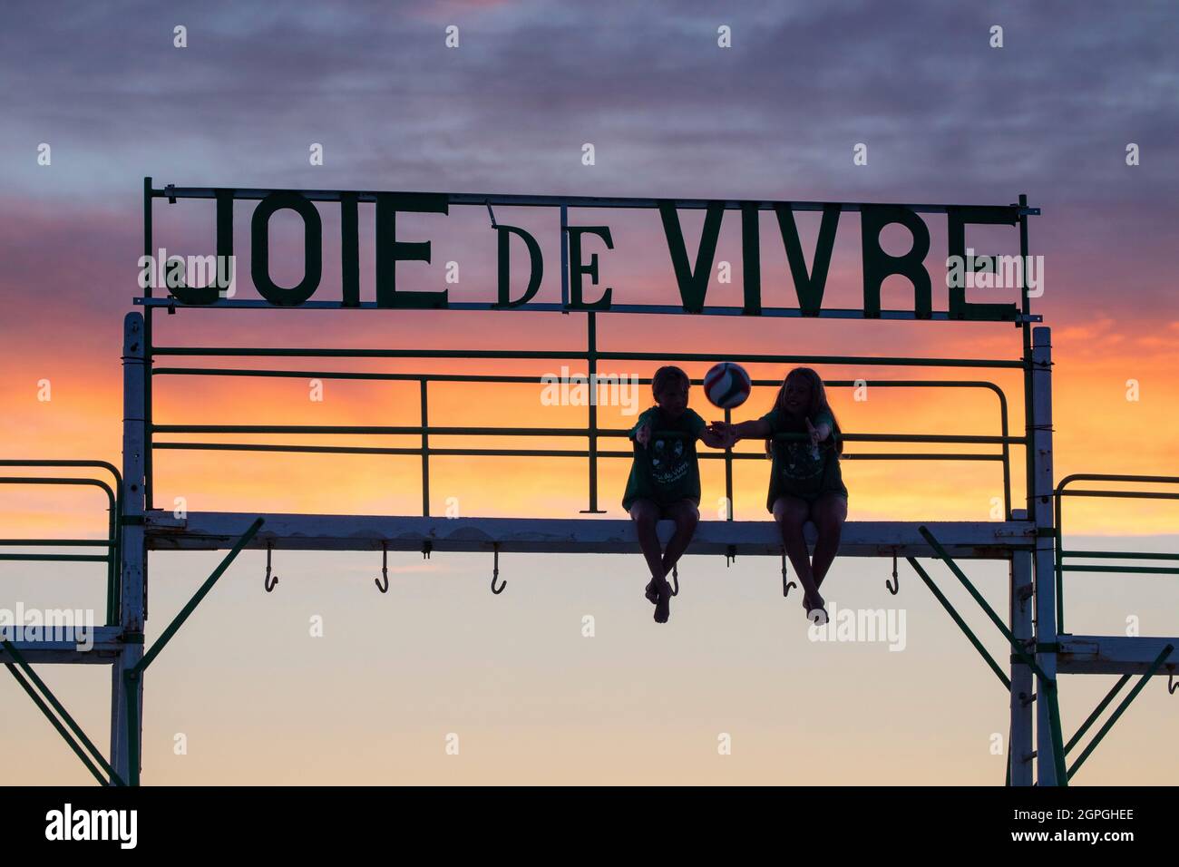 France, Pas de Calais, Cote d'Opale, Le Touquet, 2 children on the swing of the joie de vivre beach club at sunset Stock Photo