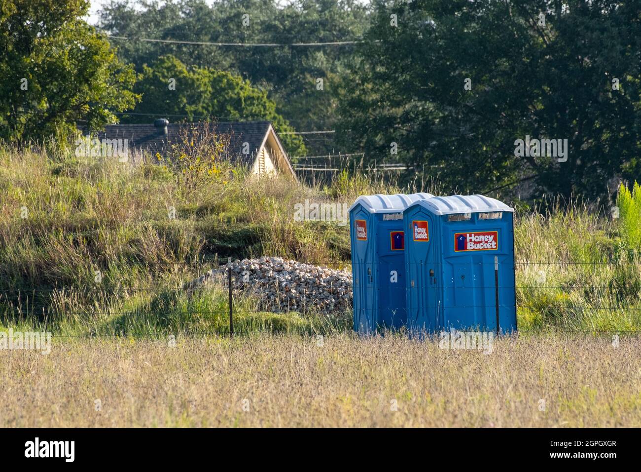 Two portable toilets' painted blue and commonly called porta-potties in US setting out in grassy field with house in background Stock Photo