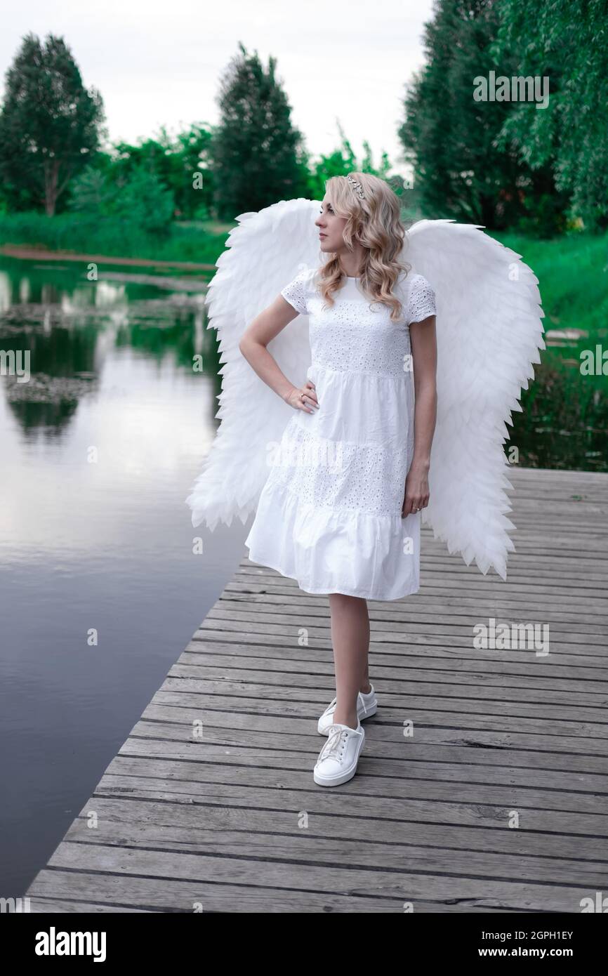 charming blonde with white angel wings standing by the water