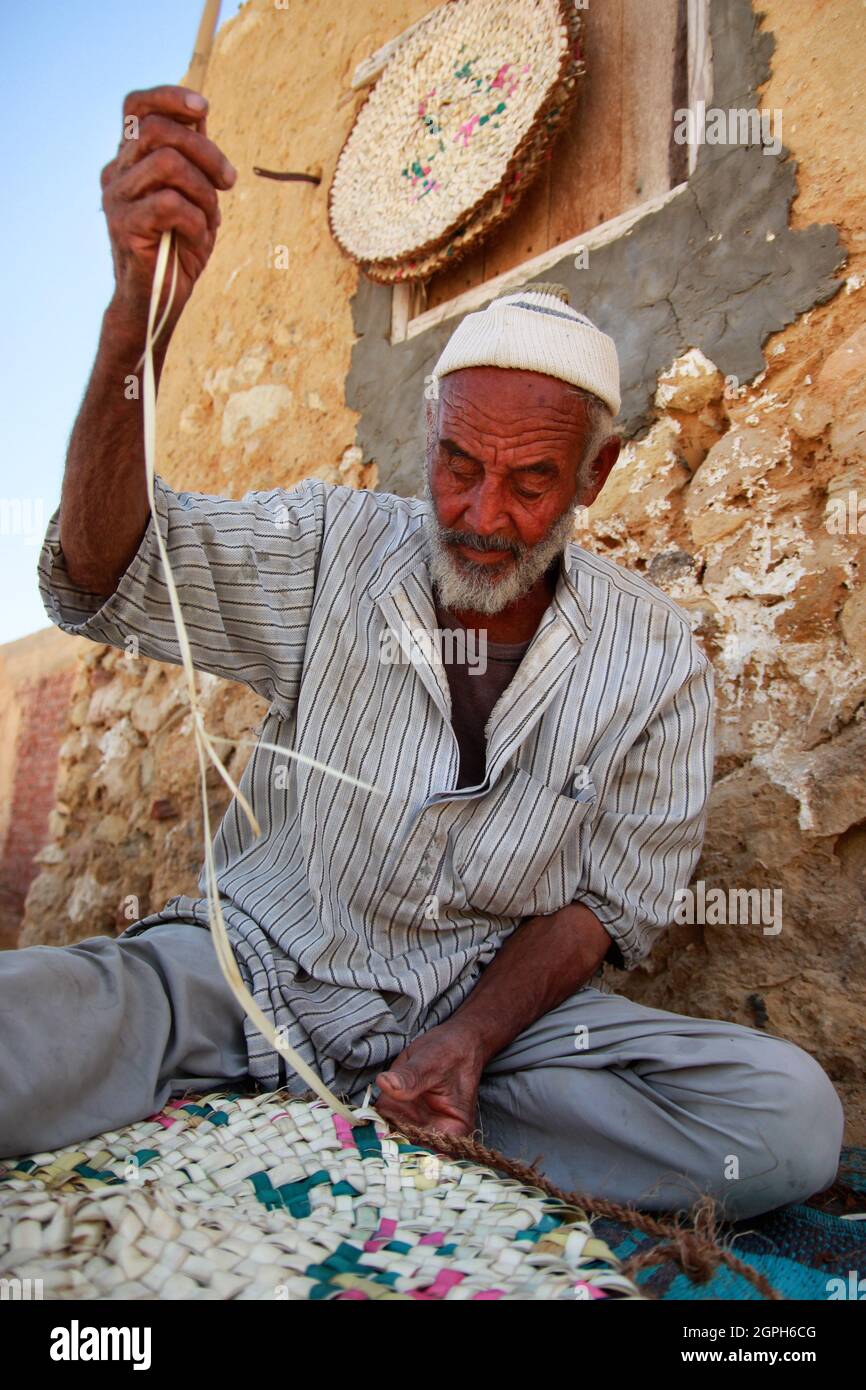A Siwan man is weaving palm leaf into traditional bags and mat. The traditional straw plaited bags are still used widely in the Oasis. Stock Photo