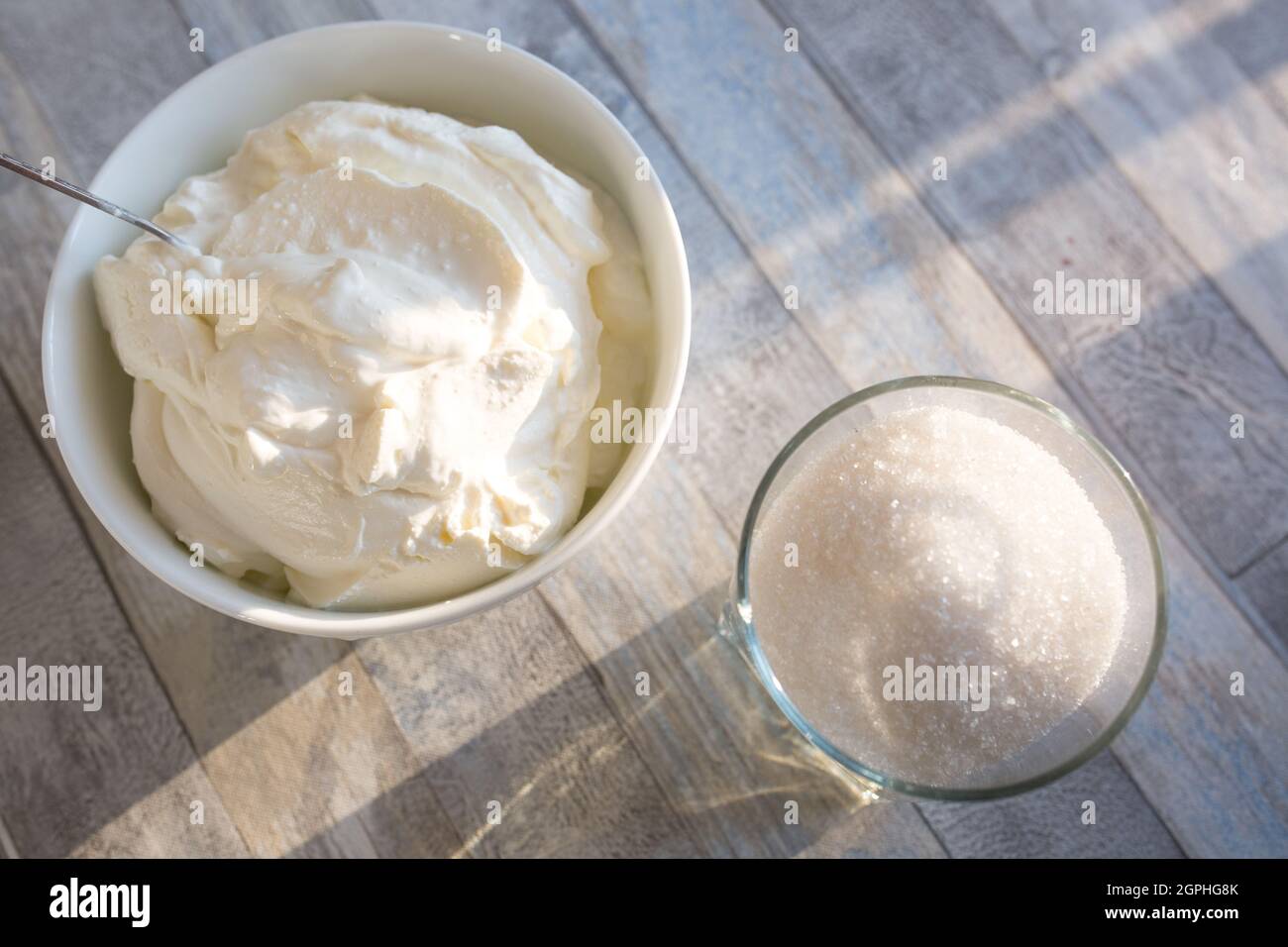 Step by step the process of making sour cream. Sour cream and sugar are prepared on a wooden table. Stock Photo