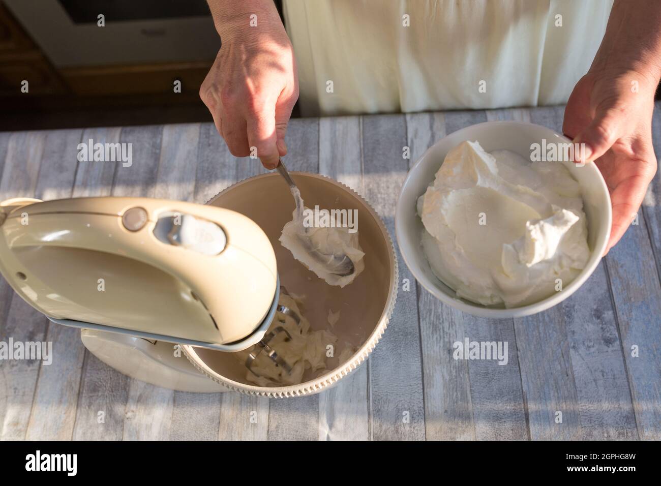 Step by step the process of making sour cream. Women's hands add sour cream to the mixer bowl for beating. Stock Photo