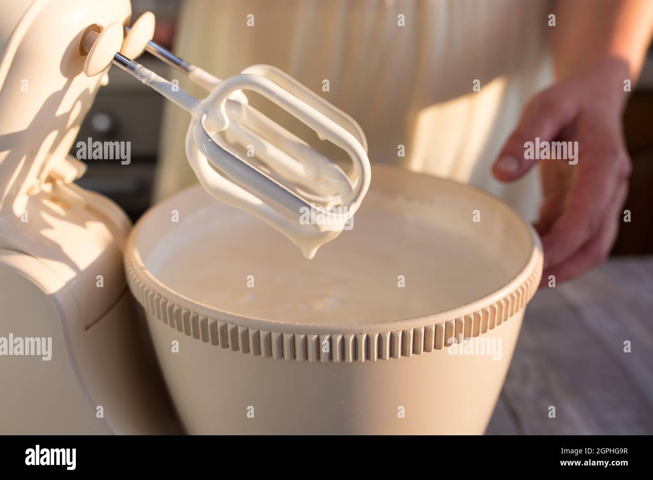 Step by step the process of making sour cream. The cream is ready. The hostess removes the mixer beaters from the container with the ready-made cream. Stock Photo
