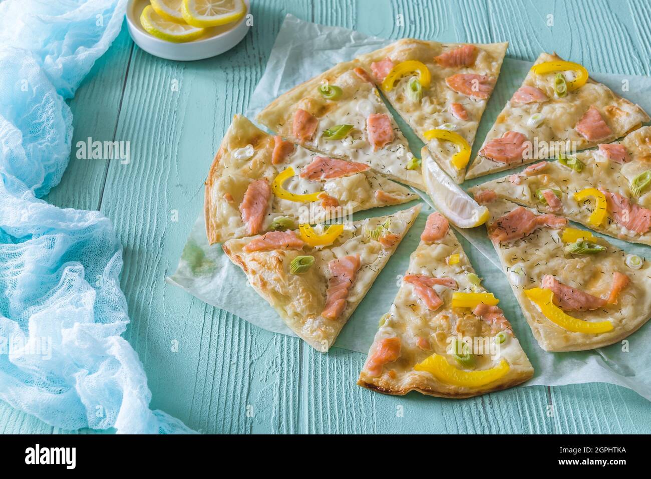 Tarte flambee with salmon, yellow pepper and spring onions on light blue background Stock Photo