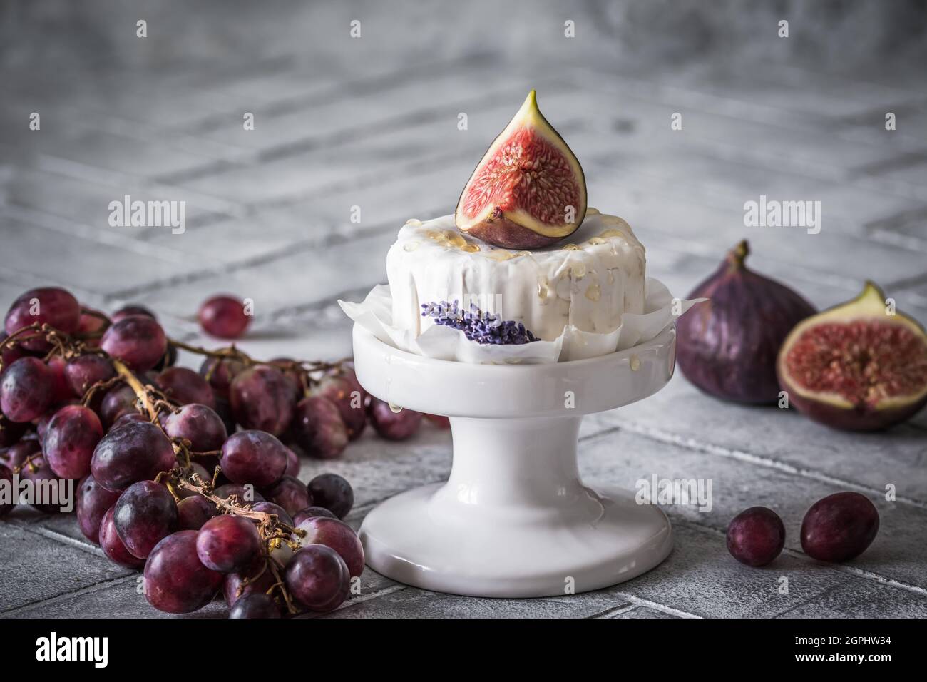 Whole round soft cheese with honey and fig on gray tiles, decorated