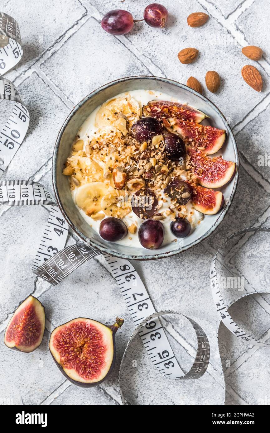 Bowl of yoghurt, fruits and nuts for a healthy diet breakfast or snack and a tape measure on gray background, weight loss concept. Top view. Stock Photo