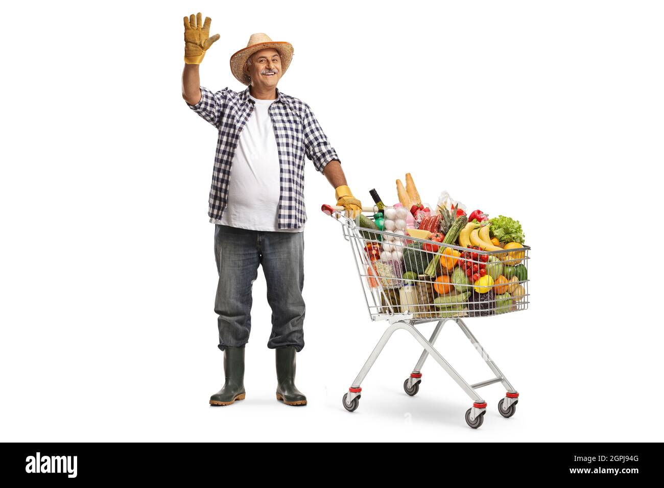 Full length portrait of a farmer with a shopping cart full of food products waving at camera isolated on white background Stock Photo