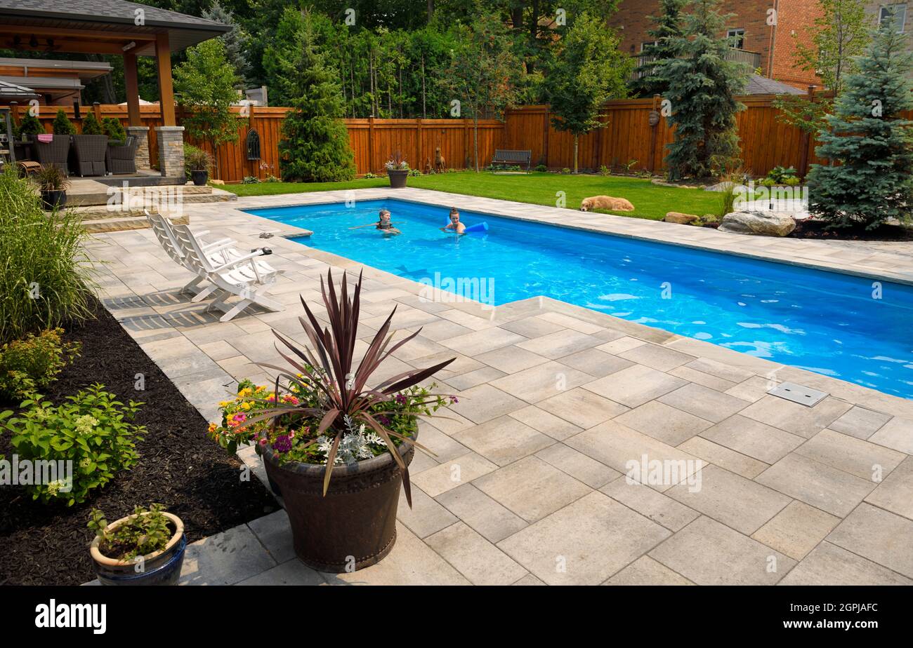 Mother and daughter swimming in new back yard pool with dog a patio of pavers and green lawn and gardens Stock Photo