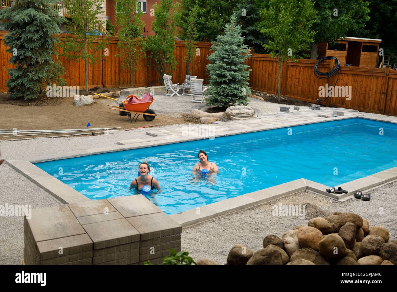Two women swimming in newly installed pool with back yard landscaping construction Barrie Ontario Canada Stock Photo